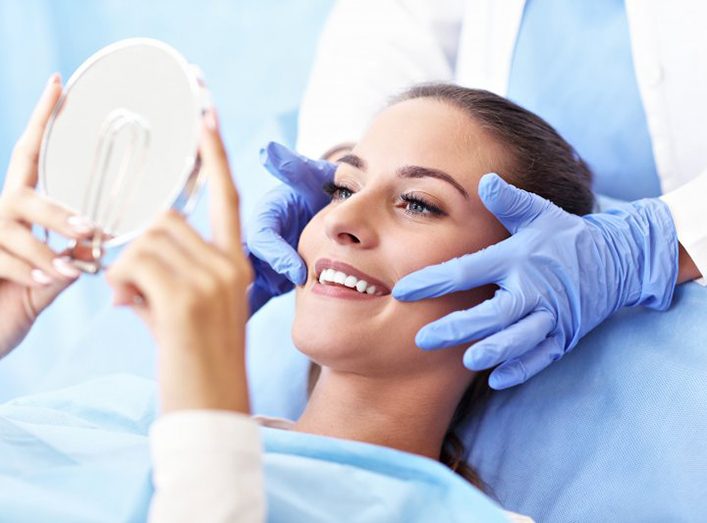 young woman admiring her new dental crowns in Granger in hand mirror 