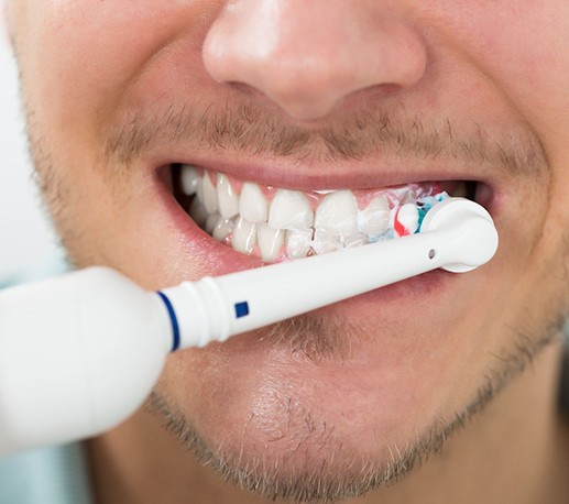 close up of man with short facial hair brushing teeth with white electric toothbrush 