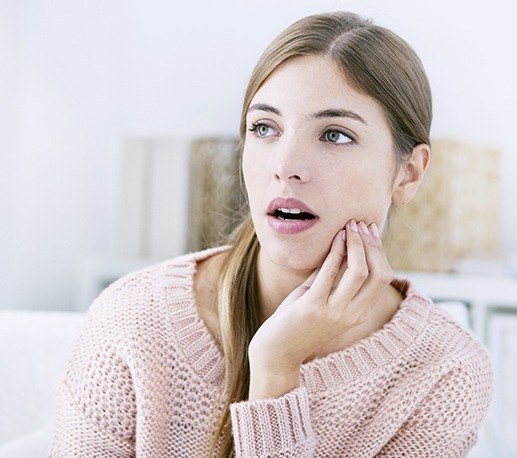 Woman holding cheek before emergency dentistry