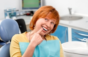 Woman pointing to smile after replacing missing teeth