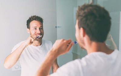 Man standing in front of mirror, brushing teeth and smiling