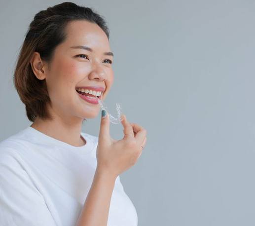 Smiling woman holding clear aligner, standing against gray background
