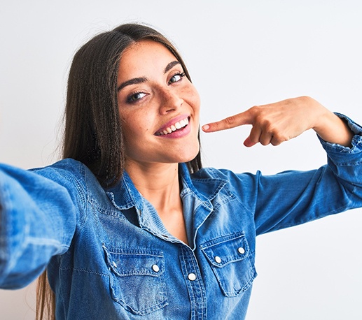 Woman pointing to her smile while wearing a long sleeve denim shirt