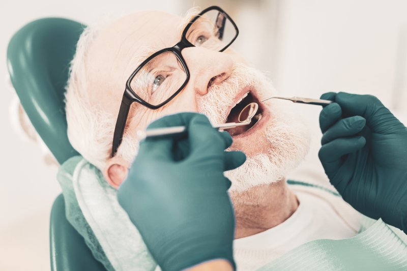 an elderly man having his teeth checked by a dentist during a six-month appointment